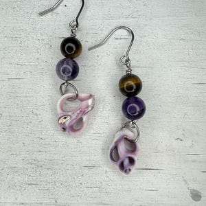 May include: A pair of dangle earrings with a purple and brown gemstone bead and a pink seashell charm.