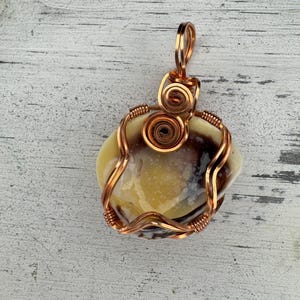 May include: A copper wire wrapped pendant featuring a yellow and brown agate stone. The pendant has a copper wire loop for hanging.
