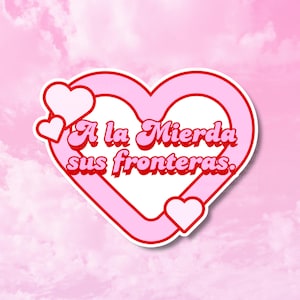 May include: A pink sticker with a heart shape and the text "A la Mierda sus fronteras" in red. The sticker has a white border and small heart accents. The background is a pink sky.