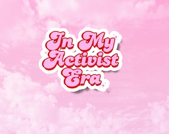 Puede incluir: Una pegatina rosa y blanca con el texto "In My Activist Era" en un estilo de fuente retro. La pegatina está sobre un fondo rosa con nubes blancas.