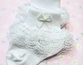 May include: White baby socks with a lace ruffle and a white satin bow. The socks are made of a soft, stretchy material and are perfect for a special occasion.