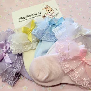 May include: Set of five baby socks with lace trim in various colors, including lavender, white, light blue, and pink. Each sock has a different colored bow.