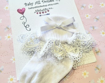 May include: White baby socks with a white lace ruffle and a white satin bow. The socks are on a white card with the text "Baby All Dolled Up babyalldolledup.etsy.com."