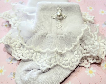May include: White baby socks with a white lace ruffle and a silver cross with a pearl embellishment.