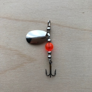 May include: A silver fishing lure with an orange bead and a treble hook.