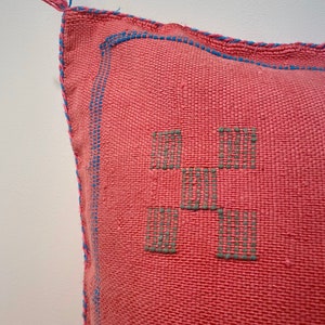 May include: A pink pillow with a blue trim and a geometric pattern in green thread.