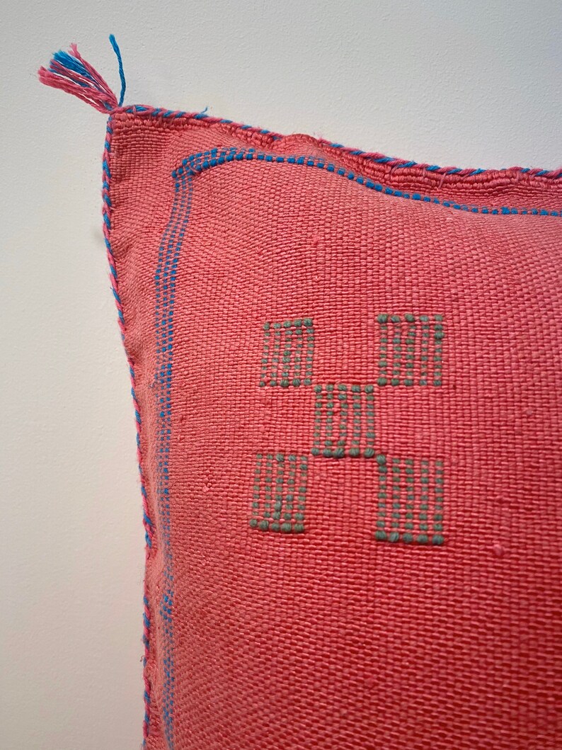May include: A pink pillow with a blue trim and a geometric pattern in green thread.
