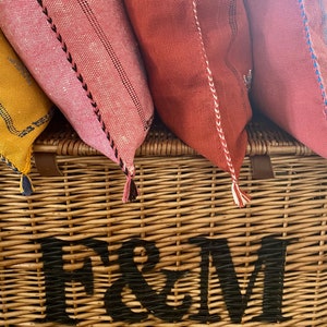 May include: Four colorful throw pillows with tassels are arranged on top of a wicker basket with the text "Fortnum & Mason" printed on the front.