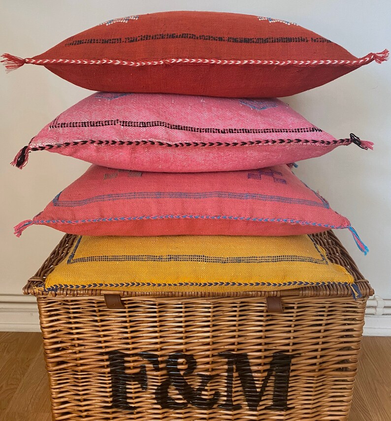 May include: Four colorful throw pillows stacked on top of a wicker basket with the letters "F&M" printed on the front.