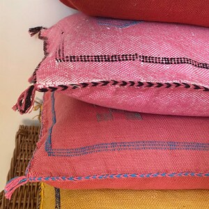 May include: A stack of four colorful throw pillows with woven patterns and tassels. The pillows are arranged on a wicker basket.