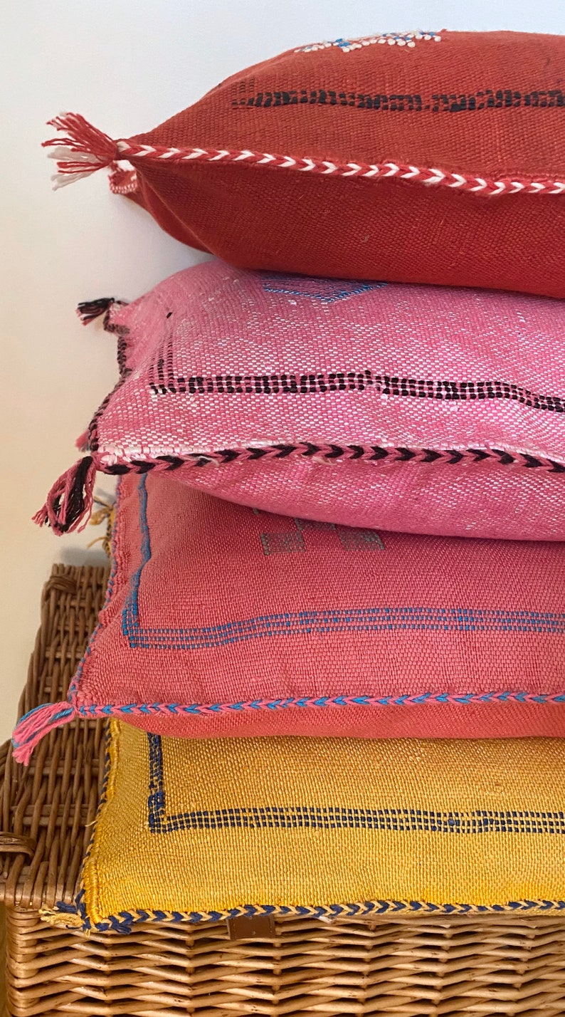 May include: A stack of four colorful throw pillows with woven patterns and tassels. The pillows are arranged on a wicker basket.