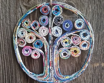 May include: A colorful paper tree wall hanging made from rolled up magazine pages. The tree is circular and has a brown wooden background.