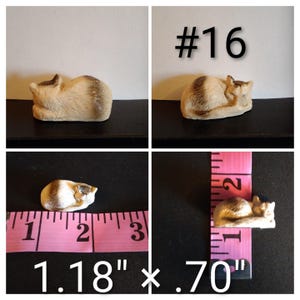 May include: A small, ceramic cat figurine in a sleeping pose. The cat is beige with brown markings and measures 1.18 inches long and .70 inches wide. The number "#16" is visible in the image.