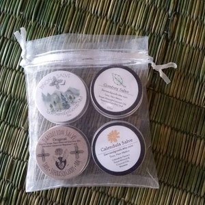 Puede incluir: Cuatro peque&ntilde;as latas redondas de b&aacute;lsamo con etiquetas que presentan un dise&ntilde;o del suroeste. Las etiquetas incluyen los nombres "Pinon Salve", "Comfrey Salve", "Dandelion Salve" y "Calendula Salve". Cada etiqueta tambi&eacute;n incluye el nombre "SierraSoGoods" y la ubicaci&oacute;n "Taos, Nuevo M&eacute;xico".