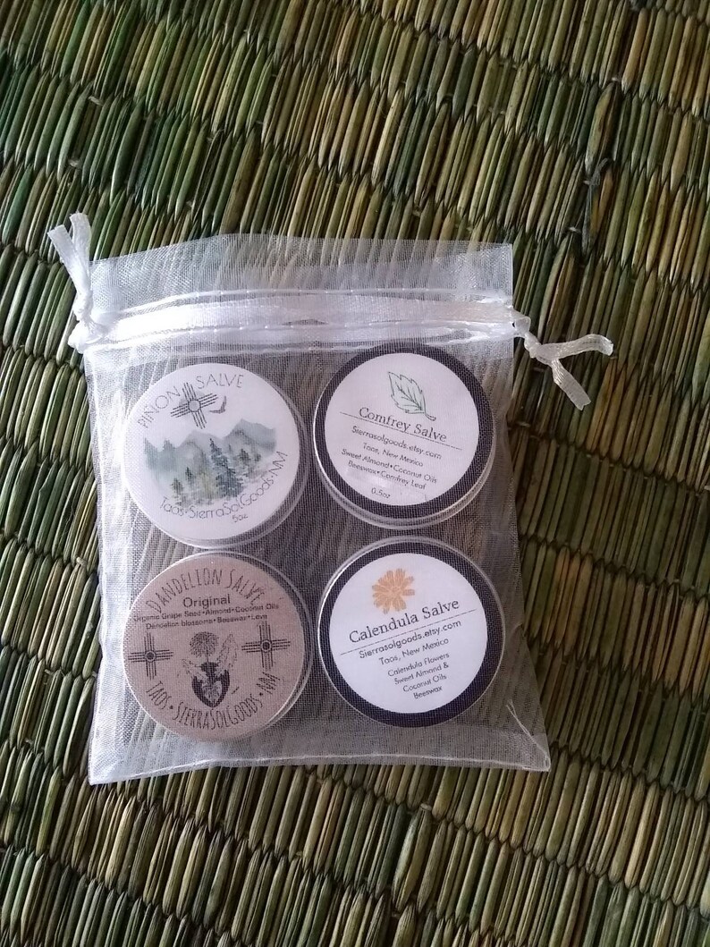 Puede incluir: Cuatro peque&ntilde;as latas redondas de b&aacute;lsamo con etiquetas que presentan un dise&ntilde;o del suroeste. Las etiquetas incluyen los nombres "Pinon Salve", "Comfrey Salve", "Dandelion Salve" y "Calendula Salve". Cada etiqueta tambi&eacute;n incluye el nombre "SierraSoGoods" y la ubicaci&oacute;n "Taos, Nuevo M&eacute;xico".