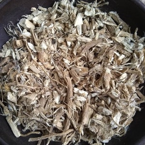 May include: A close-up of a bowl filled with dried, light brown and white root pieces. The root pieces are chopped and shredded, and some are long and thin.