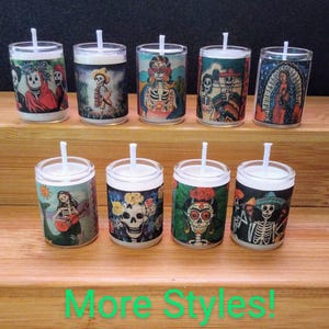 May include: Eight small glass votive candles with colorful Day of the Dead themed designs. The designs include skeletons, flowers, and religious figures. The candles are arranged in two rows on a wooden surface.  More Styles! is written in green text at the bottom of the image.