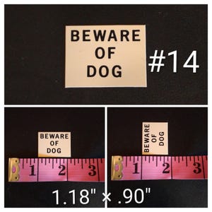 May include: A rectangular sign with the text "BEWARE OF DOG" in black capital letters. The sign is cream-colored and measures 1.18 inches by 0.90 inches. The number "#14" is in white. The sign is on a black background.