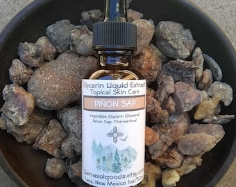 May include: A small amber glass bottle with a dropper top filled with a clear liquid. The bottle label reads "Glycerin Liquid Extract Topical Skin Care PIÑON SAP Vegetable Glycerin (Glycerol) Piñon Sap: (Trementina) Sierrasolgoods.etsy.com Taos, New Mexico 1oz/30ml". The bottle is sitting on a bed of brown, rocky, natural material.