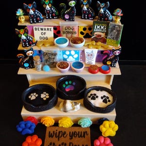 May include: A multi-tiered display of pet-themed items. The top shelf features Day of the Dead cat figurines, bowls, and signs that read "Beware of Dog" and "Dog Bones." The middle shelf has cat food and catnip. The bottom shelf has paw-shaped items.