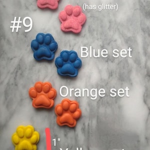 May include: A collection of colorful paw-shaped items in pink, blue, orange, and yellow. The pink set has glitter. Each paw measures 1 inch. Text on the image reads "Pink set," "Blue set," "Orange set," and "Yellow set."