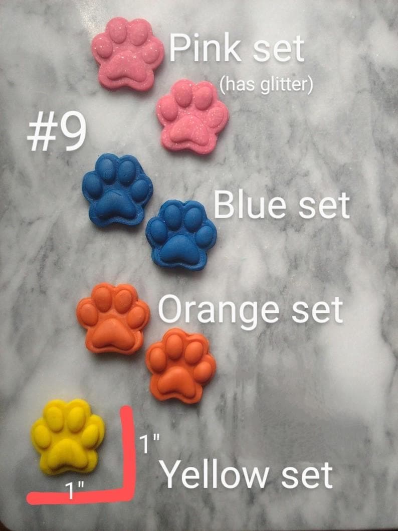 May include: A collection of colorful paw-shaped items in pink, blue, orange, and yellow. The pink set has glitter. Each paw measures 1 inch. Text on the image reads "Pink set," "Blue set," "Orange set," and "Yellow set."