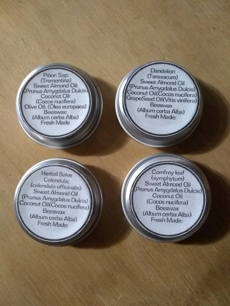 Puede incluir: Cuatro latas plateadas con etiquetas blancas que contienen diferentes b&aacute;lsamos herbales. Cada etiqueta enumera los ingredientes, incluyendo aceite de almendras dulces, aceite de coco, cera de abejas y el nombre latino de la hierba. Las etiquetas tambi&eacute;n indican "Reci&eacute;n hecho".