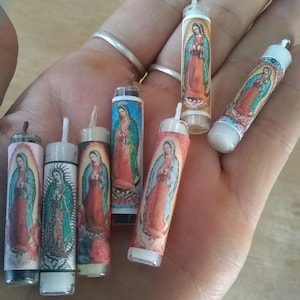 May include: A collection of small, cylindrical candles featuring images of the Virgin Mary. The candles have a clear plastic casing and are adorned with colorful religious artwork. The wicks are visible at the top of each candle.