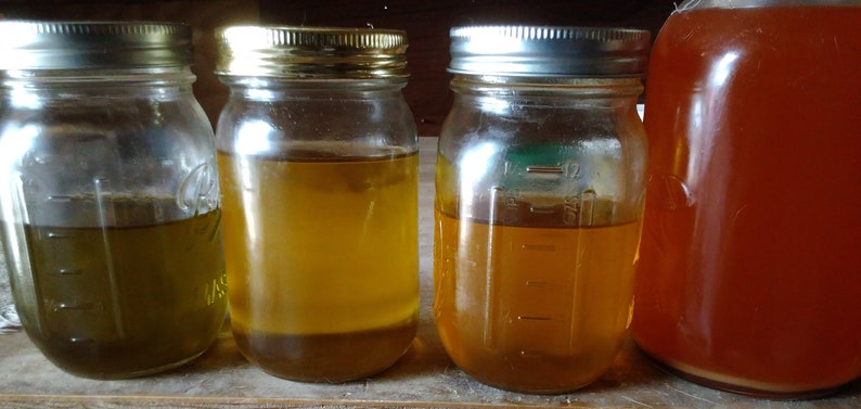 Puede incluir: Cuatro tarros de vidrio con tapas llenos de l&iacute;quidos de diferentes colores. Los tarros est&aacute;n sobre una superficie de madera. Los l&iacute;quidos son verde oscuro, amarillo claro, amarillo oscuro y naranja rojizo.