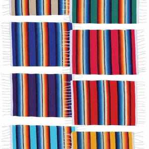 May include: A collection of rectangular woven blankets with vertical stripes in various colors. Each blanket features a different color scheme, including beige, green, blue, red, purple, and yellow, with white fringe on the short ends. The blankets are approximately 24 inches long and 12 inches wide.