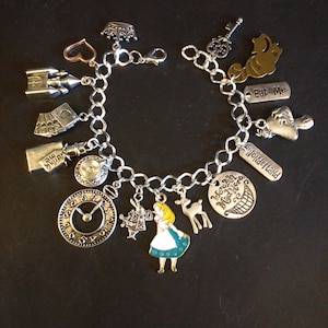 May include: Silver charm bracelet featuring Alice in Wonderland themed charms. Charms include a clock, key, crown, and Alice in her blue dress. Other charms include a deer, a Cheshire Cat, and charms with the words "Eat Me" and "Wonderland".