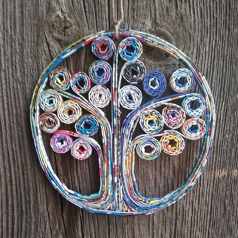 May include: A colorful paper tree wall hanging made from rolled up magazine pages. The tree is circular and has a brown wooden background.