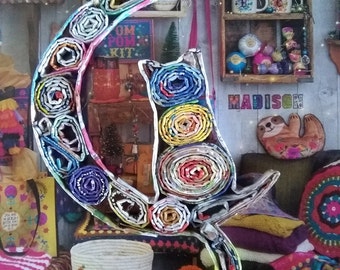 May include: A colorful cat and crescent moon sculpture made from rolled up paper. The sculpture is decorated with a variety of colors and patterns. The cat is sitting on the crescent moon and has a playful expression.