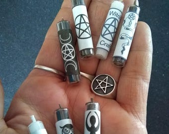 May include: A collection of small, glass vials with various occult symbols and text. The vials are white and black, with designs including pentagrams, moons, an owl, and a serpent. A silver pentagram pendant is also present.