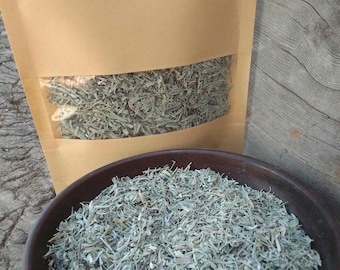 May include: A brown paper bag with a clear window containing dried sage, next to a dark brown bowl filled with sage. The bag has a white label with text that reads "Dried Big Sagebrush Wild Desert Sage (Artemisia Tridentata) Taos, NM 1oz".