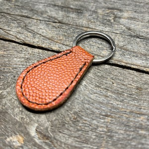 May include: A brown leather keychain with a football texture and a silver metal key ring.