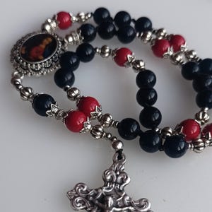 May include: A black and red rosary with a silver crucifix and a silver charm with a religious image.