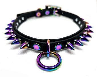 May include: A black leather choker necklace with iridescent purple spikes and a matching ring pendant. The choker features a silver buckle and rivets, and the spikes are evenly spaced around the collar.