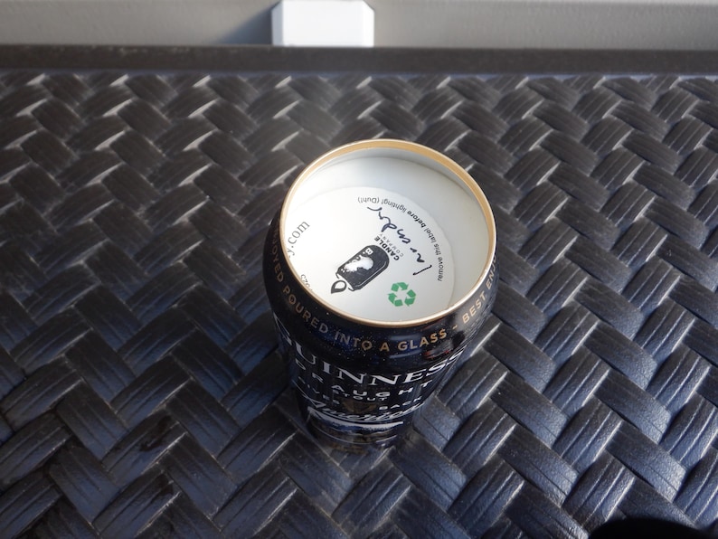 Puede incluir: Una lata plateada con una etiqueta negra y dorada que dice "Guinness" y "Draught" con un s&iacute;mbolo de reciclaje verde. La parte superior de la lata est&aacute; abierta y muestra una etiqueta blanca con el texto "I'm inside" y "Canola", con un gr&aacute;fico en blanco y negro de una lata.