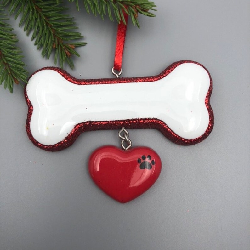 May include: White bone-shaped Christmas ornament with a red glitter trim and a red heart charm with a black paw print.