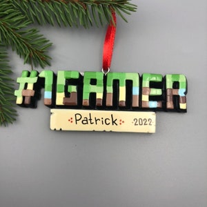 May include: A Christmas ornament with a pixelated design that says "#1 GAMER" with a banner underneath that says "Patrick - 2022".
