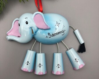 May include: Blue ceramic elephant Christmas ornament with a pink nose and ears. The elephant has a tail with a black tassel and five bells hanging from its legs. The ornament is personalised with the name "Sammy".