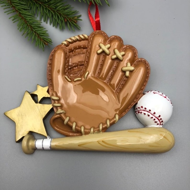 May include: A brown baseball glove with white stitching, a white baseball with red stitching, and a brown wooden baseball bat with white stripes. The glove and bat are attached to a gold star ornament.