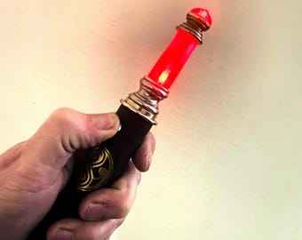 May include: A brown and gold replica of the Doctor's sonic screwdriver with a red light at the top.