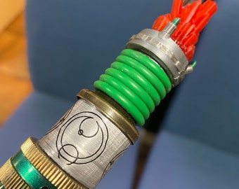May include: A close-up of a green and gold metal object with a red and white plastic top. The object has a series of green rings and a silver band with a black design.