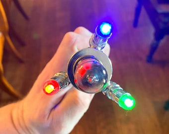 May include: A silver metal object with a clear glass bulb and four colored lights. The lights are red, yellow, blue, and green.