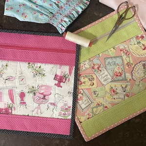 May include: Two fabric pouches with zippers, one square and one rectangular, featuring floral and polka dot patterns. The square pouch has a pink and green design with vintage labels. The rectangular pouch has a pink and white design with a pink zipper.