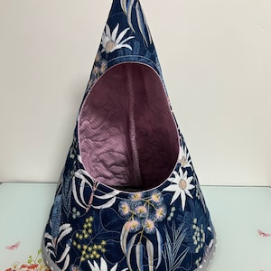 K&ouml;nnte beinhalten: Ein blaues und wei&szlig;es Blumenmuster-H&auml;ngebett f&uuml;r Haustiere mit rosafarbenem gestepptem Innenraum. Das Bett hat einen grauen und wei&szlig;en Tupfenrand.