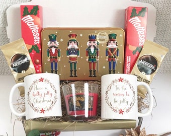 May include: A Christmas gift box with a variety of treats. Includes two white mugs with holiday text, a candle, a tin of biscuits, two boxes of Maltesers, and two packets of Nescafe coffee.