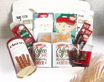 May include: A gift box filled with Christmas-themed items. Includes a tin of wafer rolls, mugs with "Running on Coffee and Christmas Cheer" text, eye masks, coffee packets, a red Radox shower gel, and a candle.
